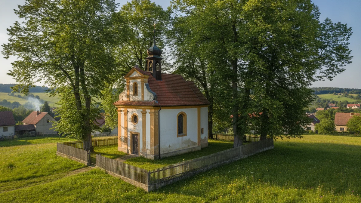 Malá barokní kaple uprostřed vesnice se vzrostlými stromy